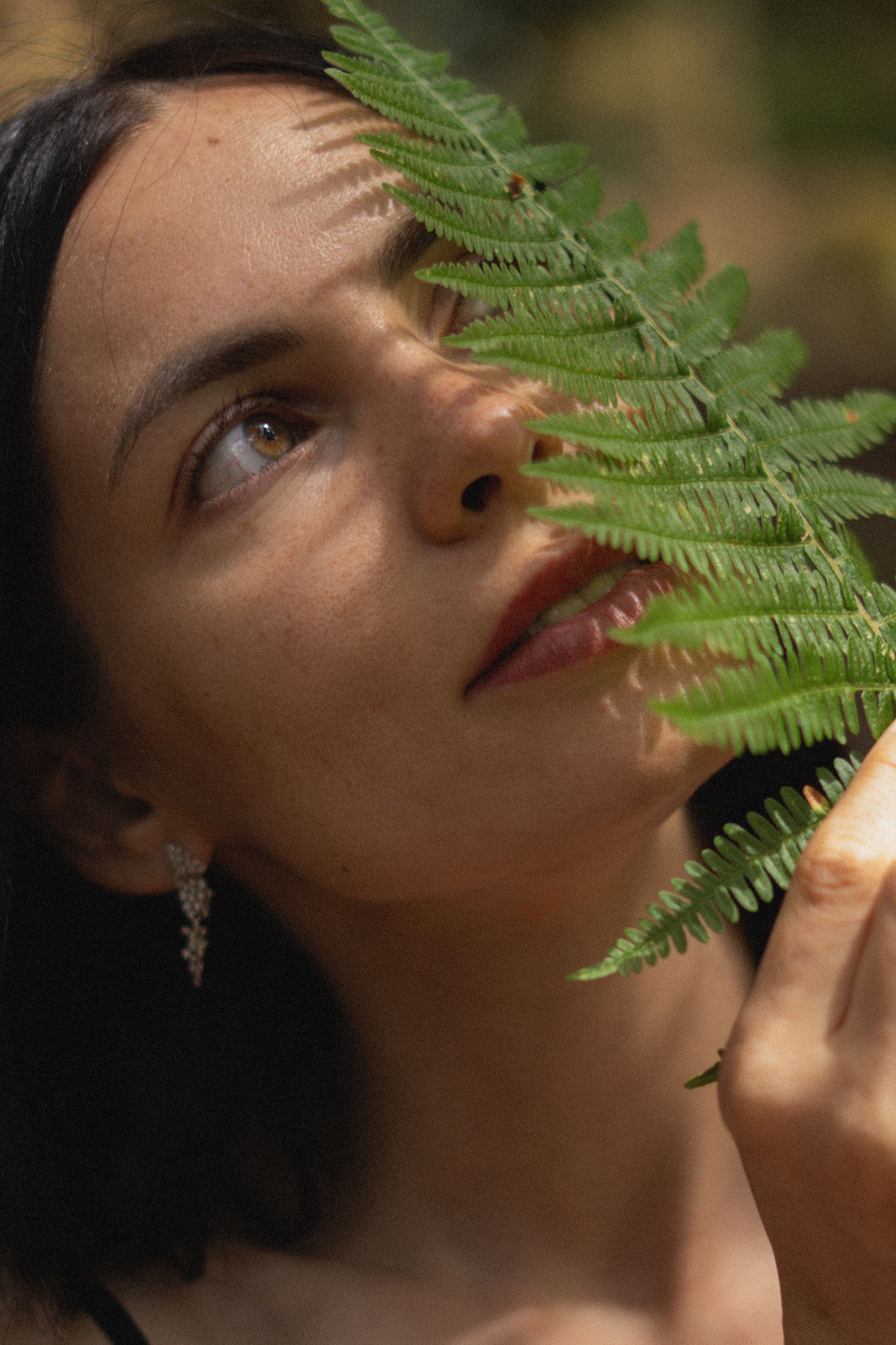 Close-up portrait of a woman behind a fern leaf