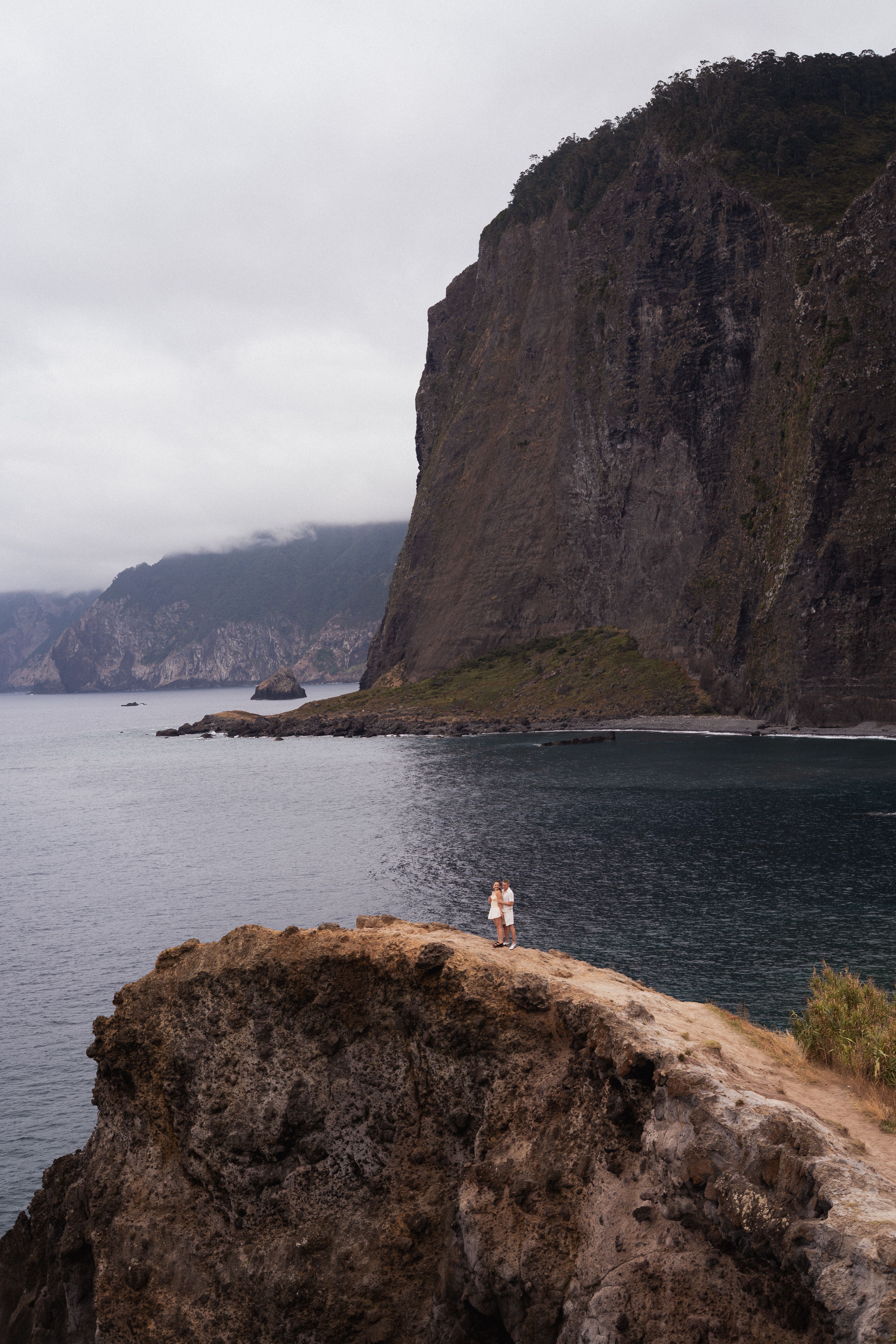 Couple standing on a cliff by the ocean beneath Madeira's high cliffs